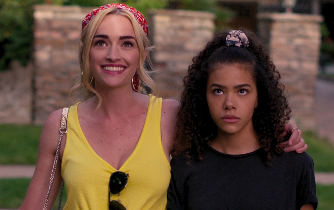 A young woman smiles while draping her arm around a frowning teenager